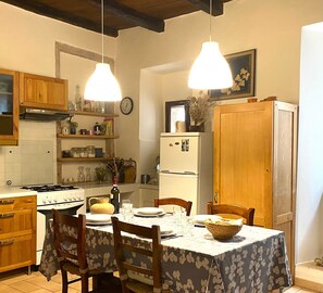 A kitchen with wooden cabinets, a stove, a refrigerator, and a dining table set for two. - Relaxation and culture, blending history and nature in Umbria’s most beautiful spots. (Acera)