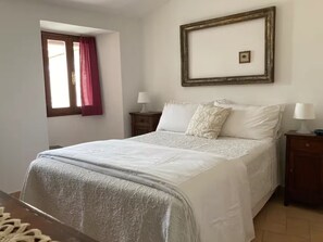 Ein Schlafzimmer mit einem Bett, zwei Nachttischen, einem Fenster mit Vorhängen und einem gerahmten Bild an der Wand.