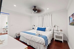 Ein Hotelzimmer mit Bett, Nachttischen, Schreibtisch, Sessel, Deckenventilator und einem Bild an der Wand.