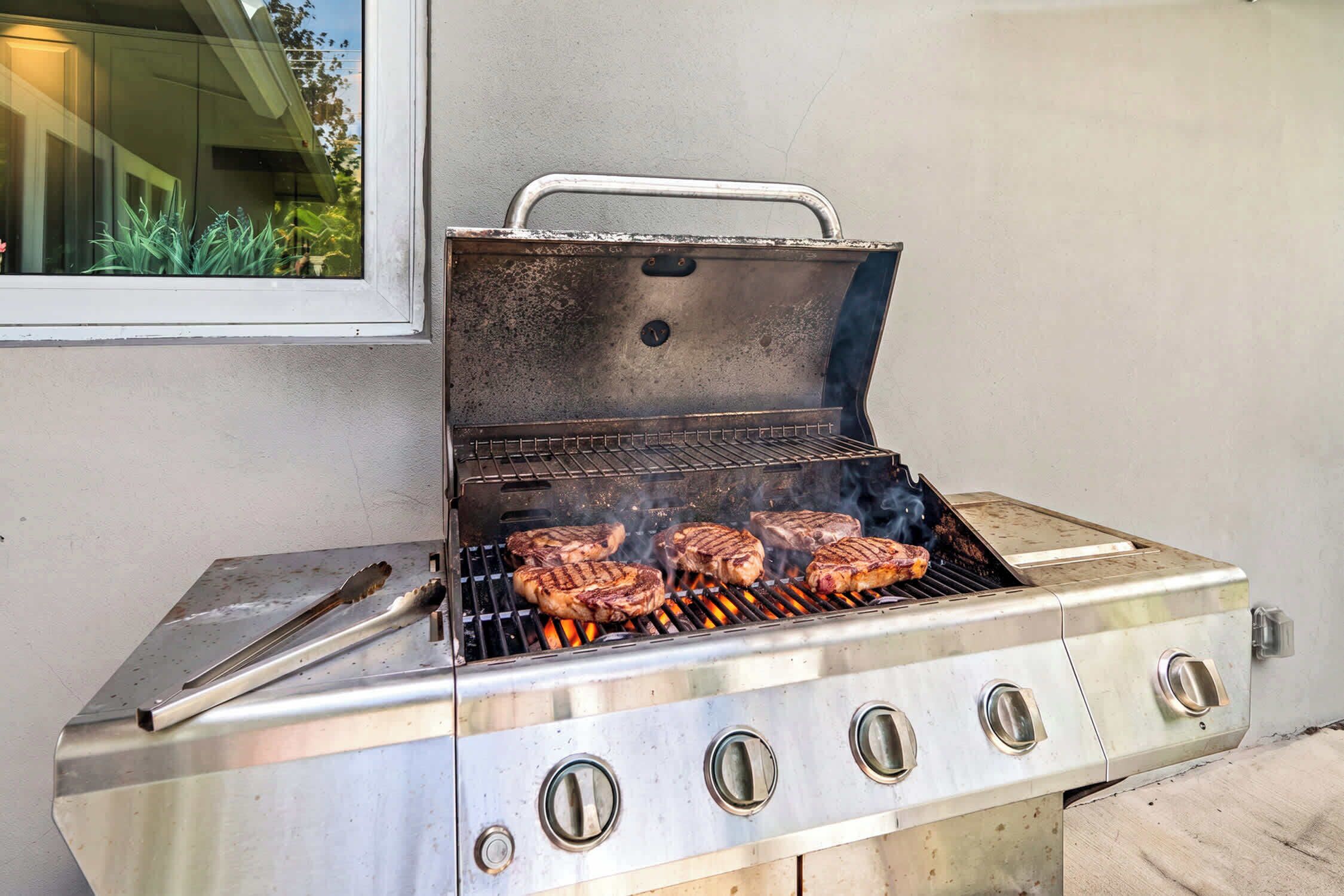 A stainless steel barbecue grill with four burners, a lid, and a handle.