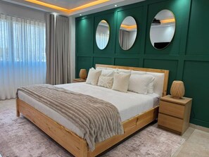 Une chambre avec un lit en bois, une table de chevet, un miroir et un mur d’accent vert.