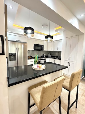 Une cuisine moderne dotée d’un îlot central, d’appareils électroménagers en acier inoxydable, de luminaires suspendus et d’un design minimaliste.