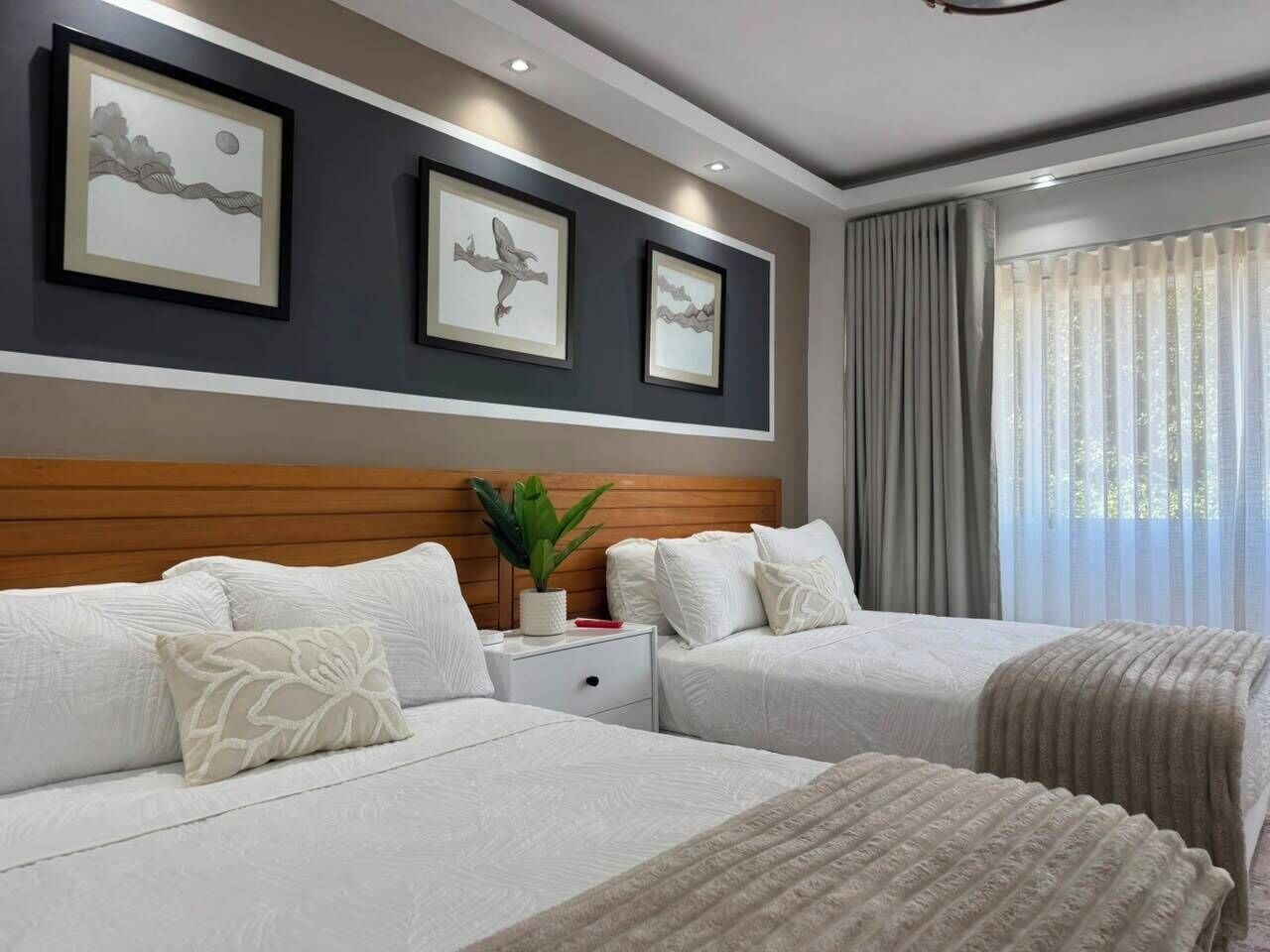 A hotel room with two beds, a wooden headboard, a nightstand with a plant, and artwork on the wall.