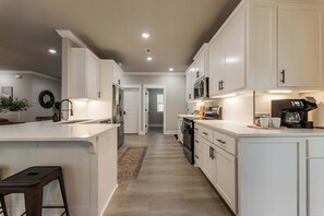 A modern kitchen with white cabinetry, a central island, and a built-in oven. - The Veloshire | Hot Tub + Back 40 Access (Bella Vista)