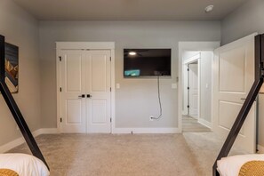 A room with a carpeted floor, two white doors, a mounted flat-screen TV, and a ceiling fan. - The Veloshire | Hot Tub + Back 40 Access (Bella Vista)