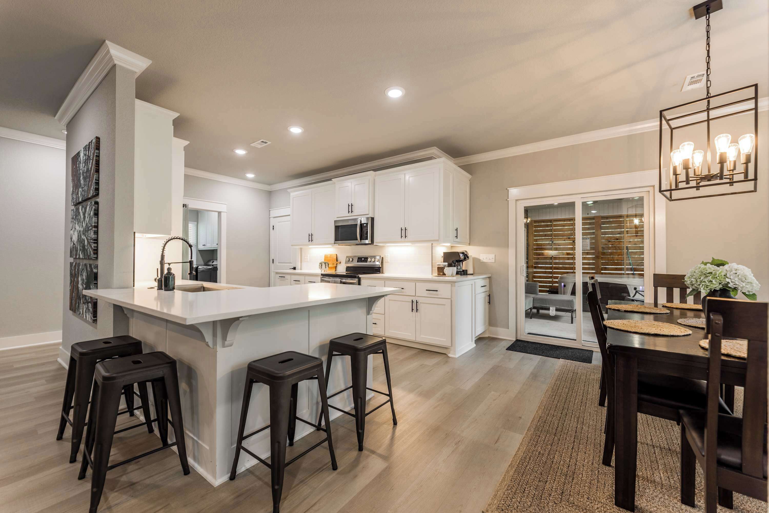 A modern kitchen with white cabinets, a central island with stools, and a dining area with a table and chairs.
