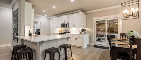 A modern kitchen with white cabinets, a central island with stools, and a dining area with a table and chairs.