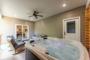 A hot tub in a covered outdoor area with a ceiling fan, a door, and a view into a house. - The Veloshire | Hot Tub + Back 40 Access (Bella Vista)