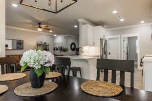 A dining area with a dark wooden table, woven placemats, and a vase of flowers. - The Veloshire | Hot Tub + Back 40 Access (Bella Vista)