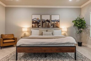 Een slaapkamer met een bed, twee bedlampen, een bankje, een stoel en een plant in pot.