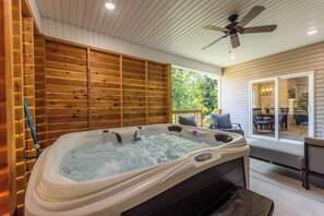 Een hottub met een houten achtergrond, een plafondventilator en uitzicht op een terras met meubilair.