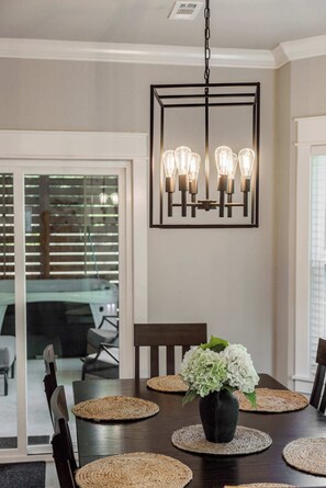 Een eetruimte met een donker houten tafel, zes stoelen en een hanglamp met meerdere lampen.