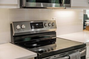 A stainless steel oven with a digital clock displaying 10:38, a control panel with multiple knobs, and a black stovetop. - The Veloshire | Hot Tub + Back 40 Access (Bella Vista)