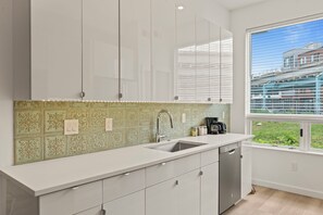 A modern kitchen with white cabinets, a patterned backsplash, a sink, and a window with a view of a building.