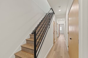 A modern staircase with wooden steps and black railings, leading to a hallway with light-colored walls and wooden flooring.