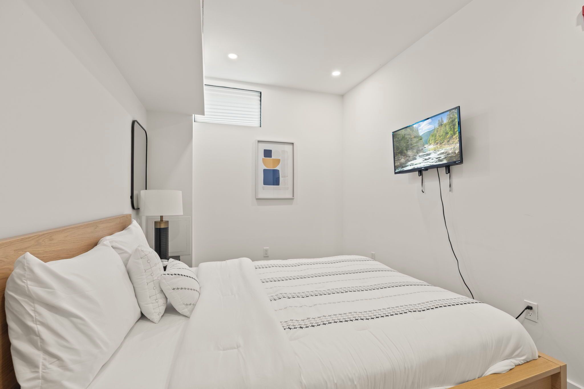 Un dormitorio moderno con una cama, un televisor de pantalla plana montado en la pared y una obra de arte abstracta enmarcada.