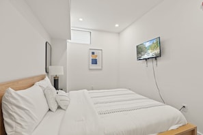 A modern bedroom with a bed, a flat-screen TV mounted on the wall, and a framed abstract artwork.