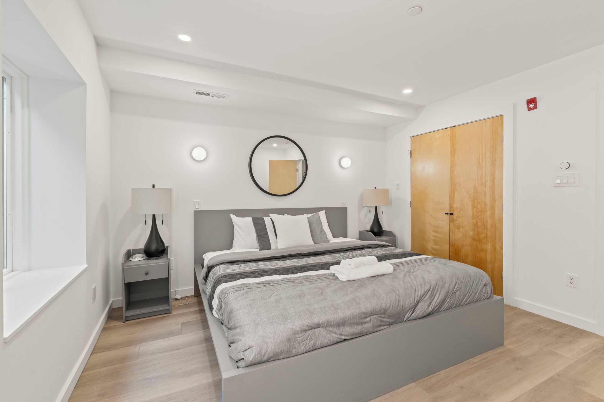 Un dormitorio moderno con una cama grande, lámparas de noche, un espejo redondo y un armario de madera.