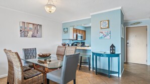 A dining area with a glass table, wicker chairs, and a kitchen in the background. - 🌊Walk 2 Beach~2 Pools~Beautiful Views~2BR The Islander 314 🌊 (Destin)