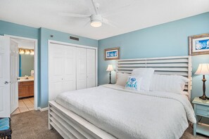 A bedroom with a bed, a ceiling fan, a door, and a nightstand with a lamp.