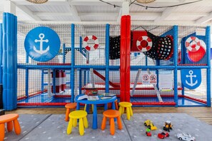 Ein Spielbereich mit einem durch ein Netz gesicherten Bereich, bunten Hockern, einem Tisch mit Spielzeug und einem Schild mit einer Rettungsboje.