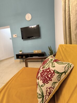 A living room with a sofa, a television mounted on the wall, a small table with a plant, and a decorative pillow. - Welcome to Su Casa, your serene escape 600m away from the sun-kissed shores (Candolim)