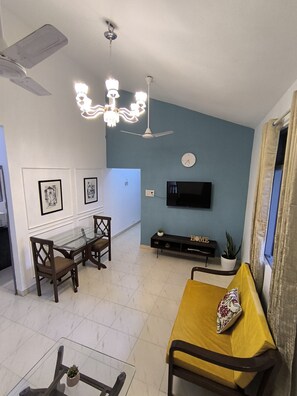 A living room with a sofa, a dining table with chairs, a TV mounted on the wall, and a ceiling fan. - Welcome to Su Casa, your serene escape 600m away from the sun-kissed shores (Candolim)