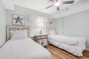 Quarto com duas camas de solteiro, uma mesa de cabeceira com luminária e um ventilador de teto.