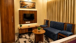 A living room with a sofa, TV, wooden cabinet, and a patterned floor. - Hotel Rai Regal (Varanasi)