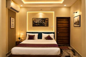 A hotel room with a bed, a wall-mounted air conditioner, a framed picture, and a door. - Hotel Rai Regal (Varanasi)