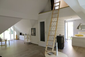 A spacious loft bedroom with a high ceiling, a wooden ladder, a bed with a yellow pillow, a desk with a lamp, and a large window. - Holiday Home Alte Schusterei with Garden, Barbecue Area and Sun Loungers (Badenweiler)