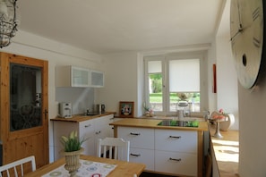 A compact kitchen with a wooden table, white cabinets, a coffee machine, and a window with blinds. - Holiday Home Alte Schusterei with Garden, Barbecue Area and Sun Loungers (Badenweiler)