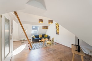 A modern loft with a sloped ceiling, a blue sofa, a wooden coffee table, and a TV on a wooden stand. - Holiday Home Alte Schusterei with Garden, Barbecue Area and Sun Loungers (Badenweiler)