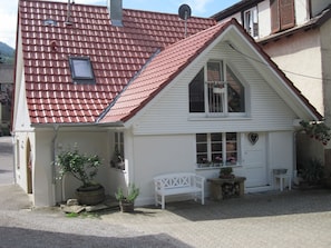 A house with a red-tiled roof, a white exterior, a small porch with a bench, and a heart-shaped decoration on the wall. - Holiday Home Alte Schusterei with Garden, Barbecue Area and Sun Loungers (Badenweiler)