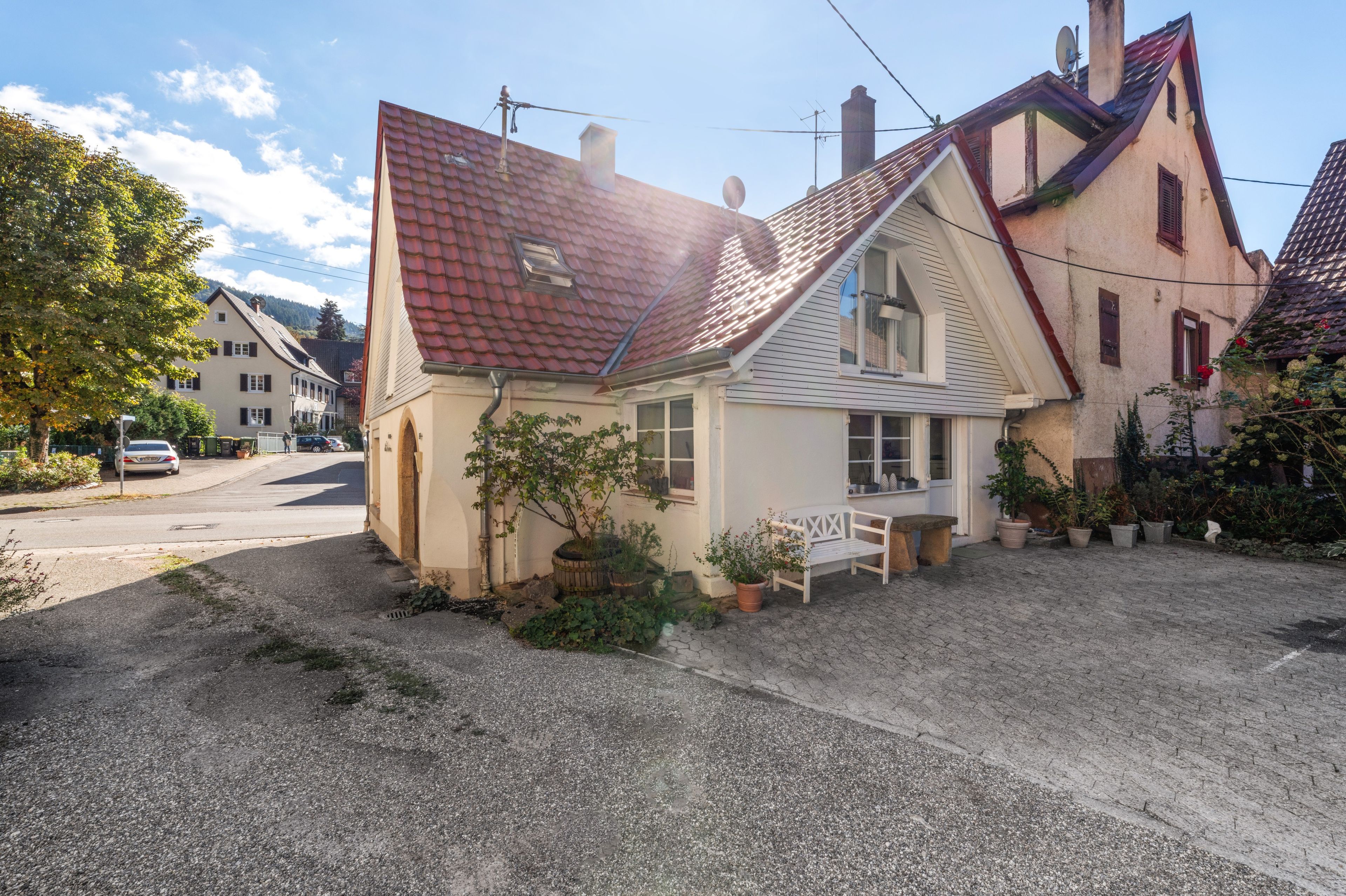 A house with a sloped roof, a small porch with a bench, and potted plants.