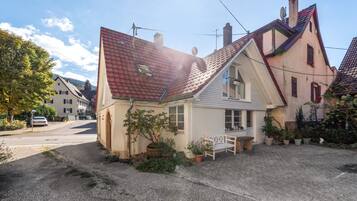 A house with a sloped roof, a small porch with a bench, and potted plants.