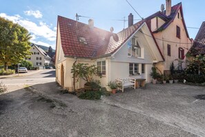 A house with a sloped roof, a small porch with a bench, and potted plants. - Holiday Home Alte Schusterei with Garden, Barbecue Area and Sun Loungers (Badenweiler)
