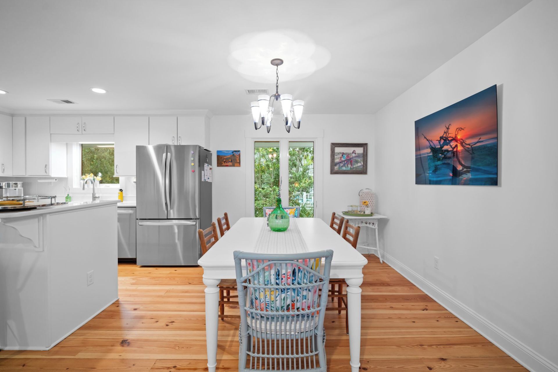 A modern kitchen with a stainless steel refrigerator, wooden flooring, and a dining area with a white table and chairs.