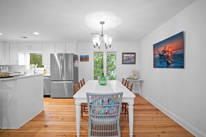 A modern kitchen with a stainless steel refrigerator, wooden flooring, and a dining area with a white table and chairs. - Charming Oceanview Beach Retreat (Fripp Island)