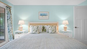 A bedroom with a large bed, two bedside tables with lamps, a framed picture on the wall, and a door.