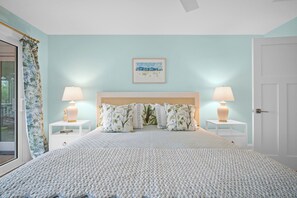 A bedroom with a large bed, two bedside tables with lamps, a framed picture on the wall, and a door. - Charming Oceanview Beach Retreat (Fripp Island)