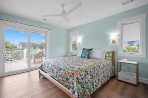 A bedroom with a bed, a nightstand, a ceiling fan, and a view of the outdoors. - Charming Oceanview Beach Retreat (Fripp Island)