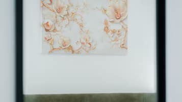 Una cama con ropa de cama blanca y un cabecero gris en una habitación con una obra de arte colgada en la pared.