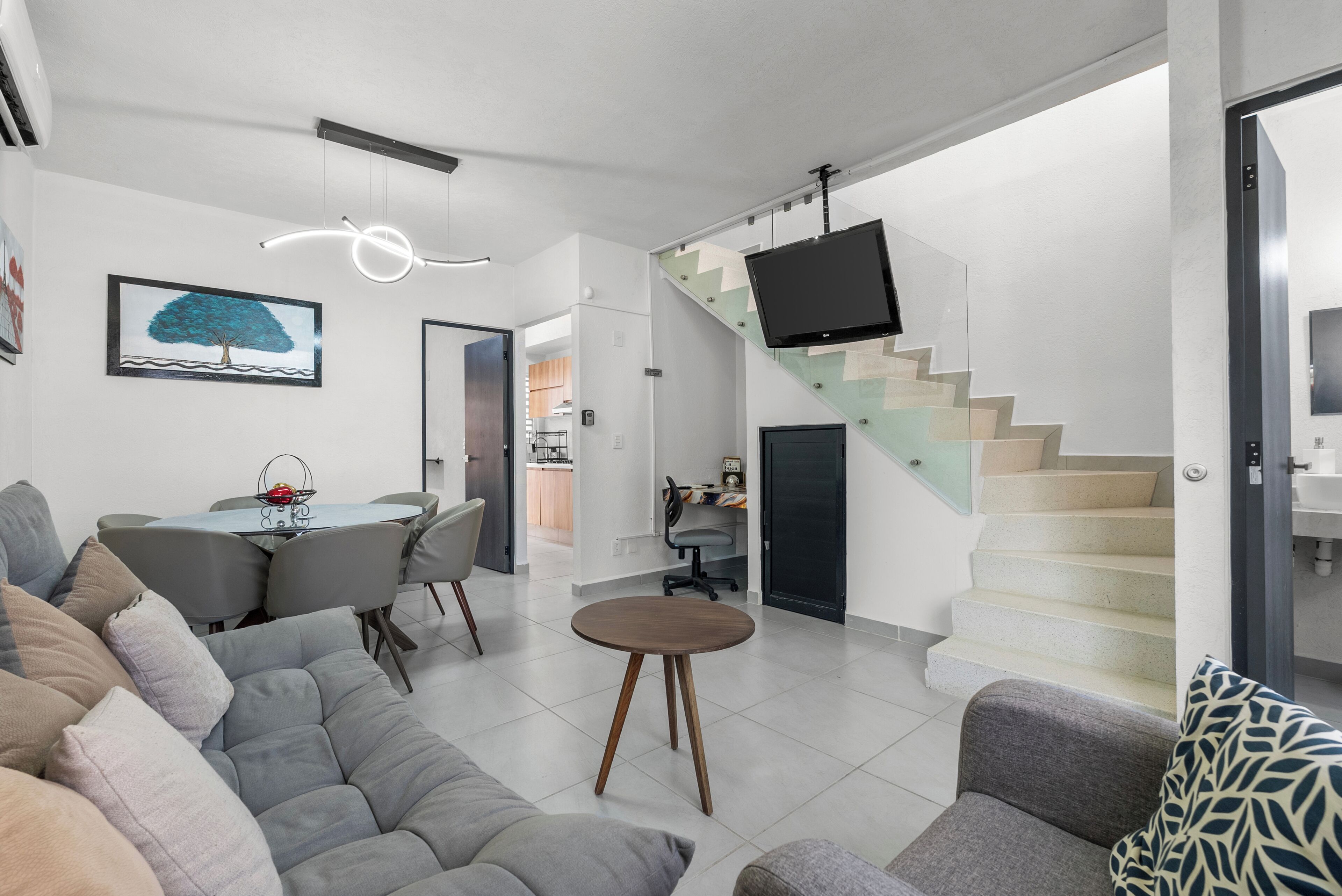 Un salon moderne comprenant un canapé, une table à manger et un escalier, avec un téléviseur.