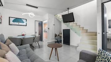 A modern living room with a sofa, a dining table, and a staircase with a TV.