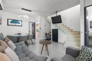 A modern living room with a sofa, a dining table, and a staircase with a TV. - Casa Esperanza Zafiro Residencial (San Vicente)