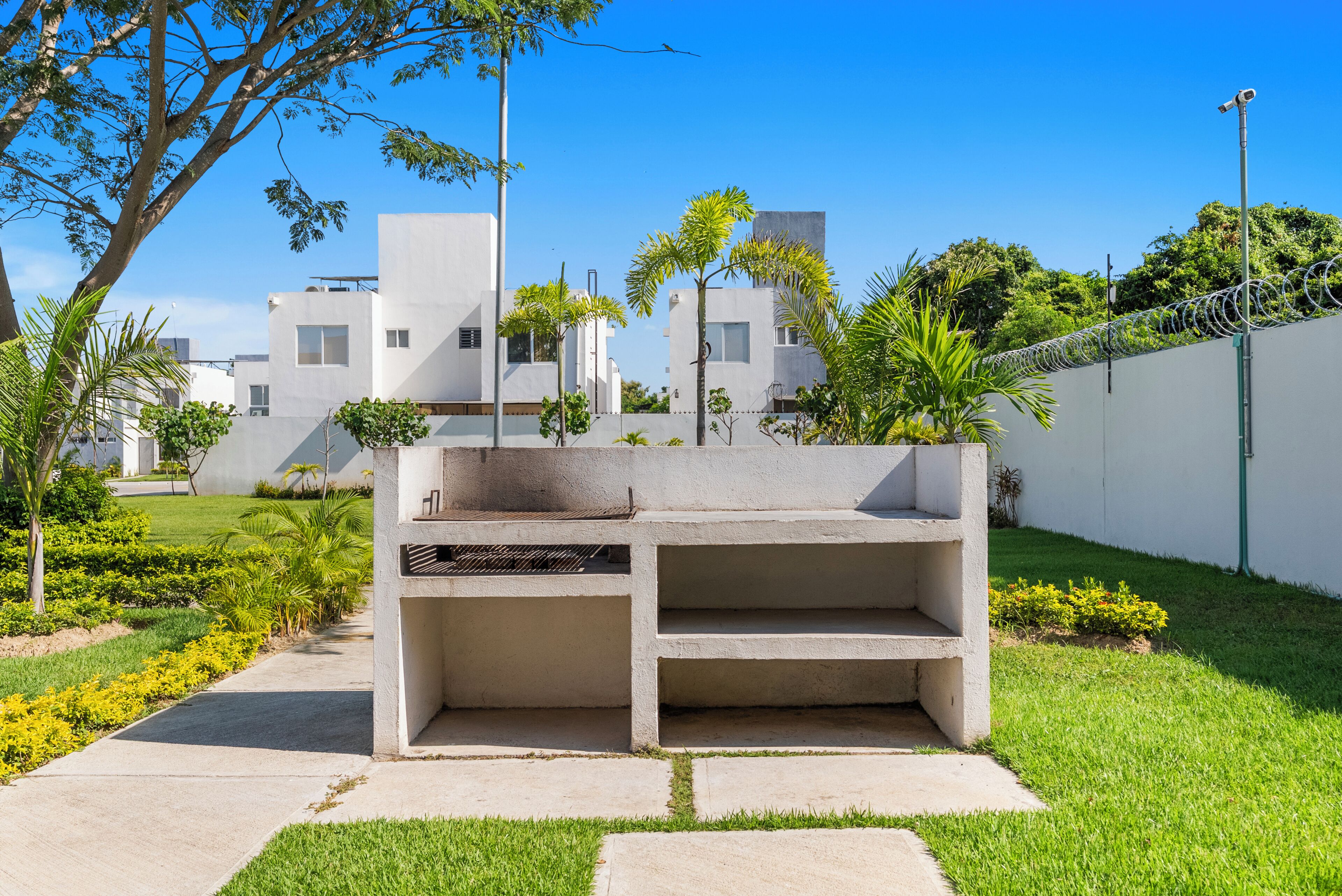 Een uitgestort terras met een bank en een tafel, omringd door groen en een wit gebouw op de achtergrond.