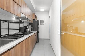 Una cuina estreta amb armaris de fusta, un rentapeus d'acer inoxidable i un frigorífic negre.