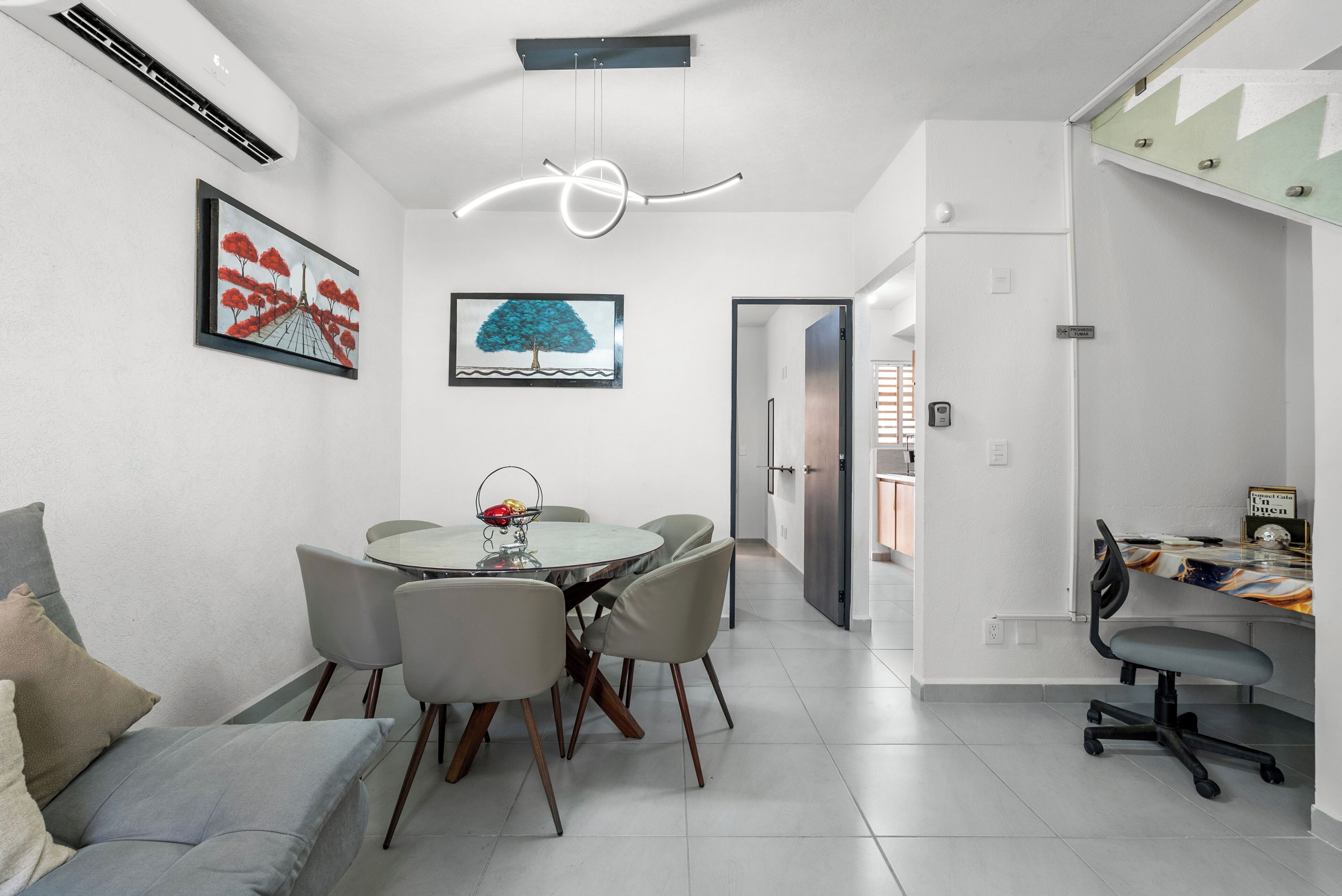 A modern dining area with a round table, grey chairs, and a ceiling light fixture.