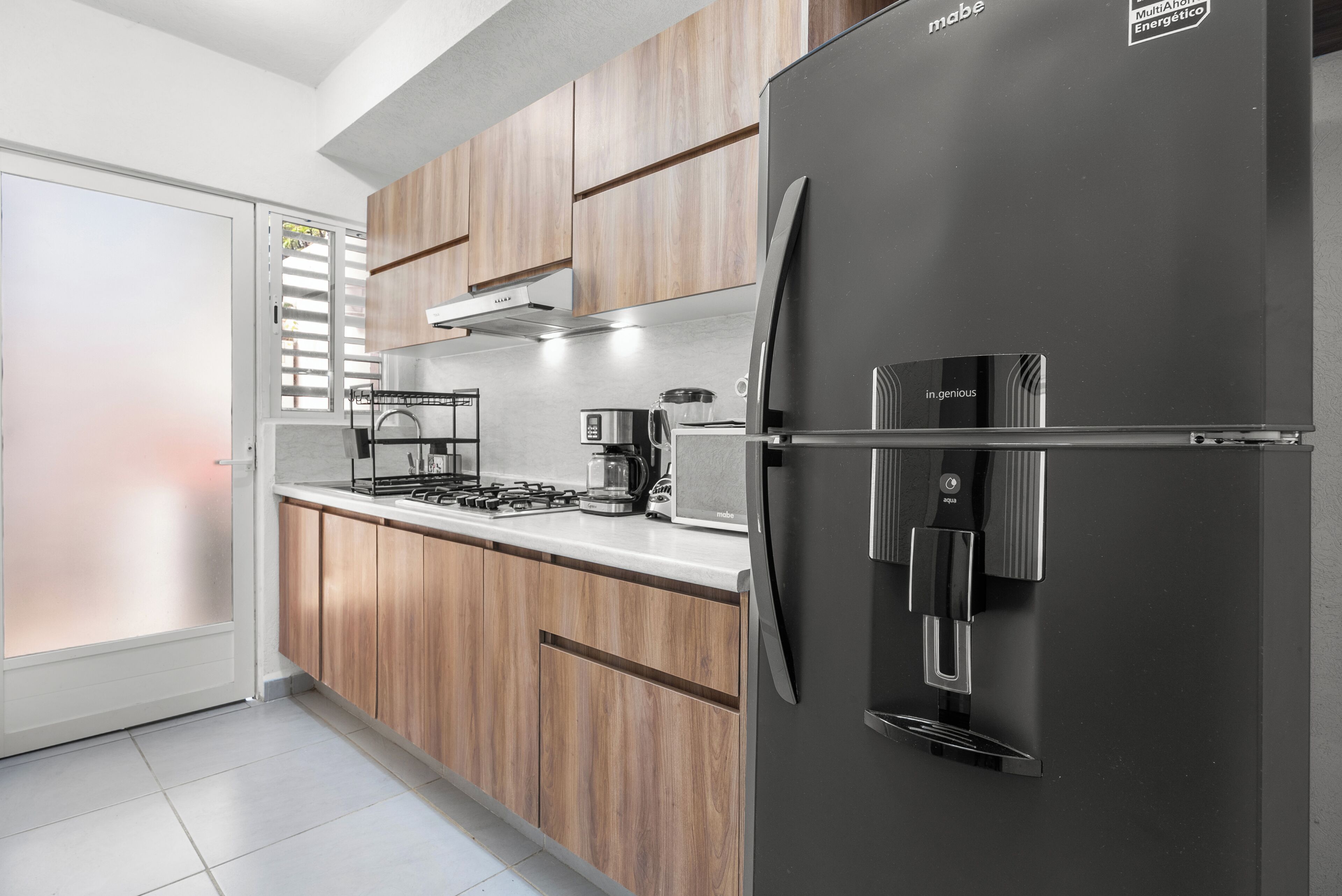 A modern kitchen with wooden cabinets, a stainless steel refrigerator, a gas stove, and a coffee maker.